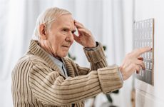 Old man touching his forehead standing infront of an button panel